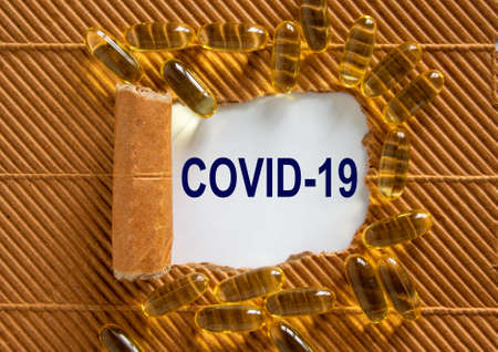 The text 'covid-19' appearing behind torn brown paper. Yellow pills. COVID-19 Pandemic Coronavirus...