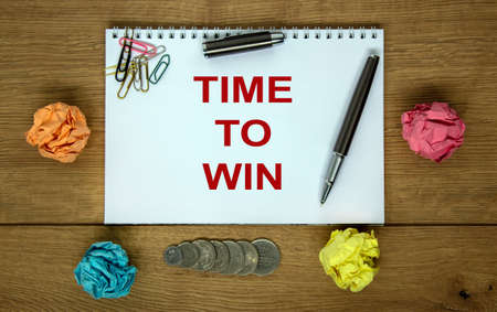 White note with inscription 'time to win' on beautiful wooden table, colored paper, coins, pen, cap and colored paper clips. Business concept.の写真素材
