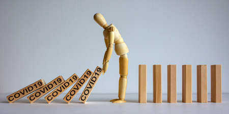 COVID-19 Pandemic Coronavirus concept. Wooden model of man stopping wooden domino blocks with...