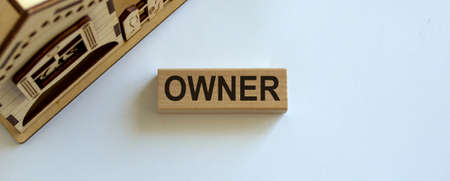 Wooden block form the word 'owner' near miniature house. Beautiful white background, copy space.の写真素材