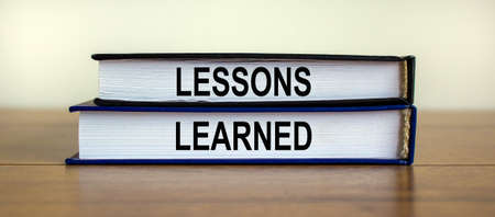 Books with text 'lessons learned' on beautiful wooden table. White background. Business concept.の写真素材