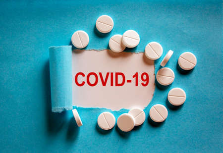 COVID-19 Pandemic Coronavirus concept. The text 'covid-19' appearing behind torn blue paper. White pills.の写真素材