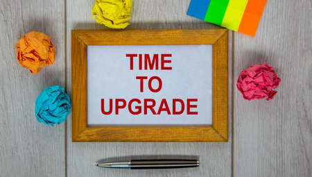Wooden picture frame with inscription 'time to upgrade' on beautiful white wooden table, colored paper and metalic pen. Business concept.の写真素材
