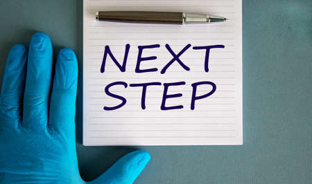 Hand in blue glove, pen, white note with words 'next step'.の写真素材