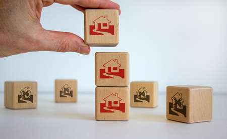 Male hand placing a cube with house sign on top of a other cubes. Cubes with abandoned house icons. The concept of overcoming the crisis. Beautiful white background.の写真素材