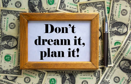 Wooden picture frame with inscription 'don't dream it, plan it' on beautiful background from dollar bills and metalic pen. Concept.の写真素材