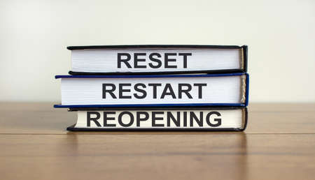 Books with text 'reset, restart, reopening' on beautiful wooden table. White background. Business concept.の写真素材