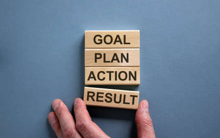 Wooden blocks form the words 'goal, plan, action, result' on blue background. Male hand.の写真素材
