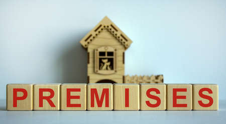 Wooden cubes form the word 'premises' near miniature house. White table. Beautiful white background, copy space.の写真素材
