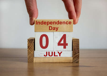 Male hand puts a block with the inscription 'Independence Day' on cubes with the date July 04th. Wooden table. Beautiful white background, copy space.の写真素材