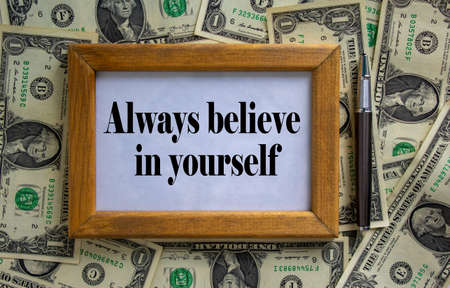 Wooden picture frame with inscription 'always believe in yourself' on beautiful background from dollar bills and metalic pen. Concept.の写真素材