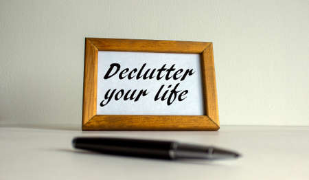 Wooden picture frame with inscription 'declutter your life' on beautiful white fon. Pen on the table.の写真素材