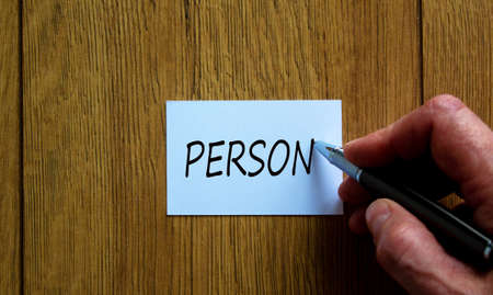Male hand writes the words 'person' on a white card. Beautiful wooden table.の写真素材