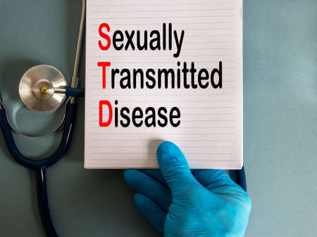Hand in blue glove with stethoscope, white card with words 'sexually transmitted disease'. COVID-19 pandemic concept.の写真素材