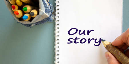 Hand writing 'our story', isolated on blue background. Bag with pencils.の写真素材