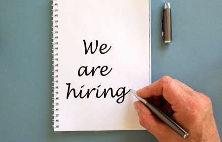 Hand writing 'we are hiring' on white note, isolated on blue background.の写真素材