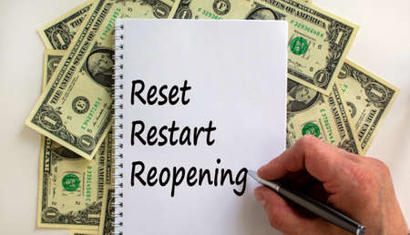 Male hand writing 'reset, restart, reopening' on white note, on white background. Dollar bills.の写真素材