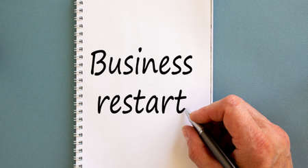 Male hand writing ' business restart' on white note, isolated on blue background.の写真素材