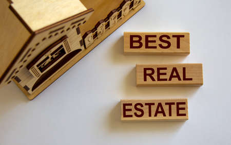 Wooden blocks form the words 'best real estate' near miniature house. White background.の写真素材