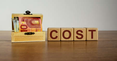 Concept word 'cost' on cubes on a beautiful wooden table, small chest with euro bills.の写真素材