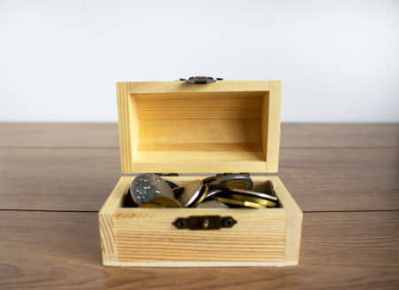 Concept business image. Small chest with coins on a beautiful wooden table. White background, copy space.の写真素材