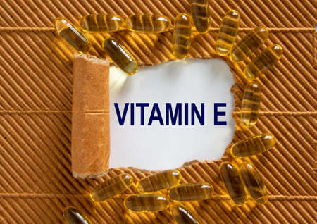 The text 'vitamin e' appearing behind torn brown paper. Yellow pills. Concept. Beautiful background.の写真素材