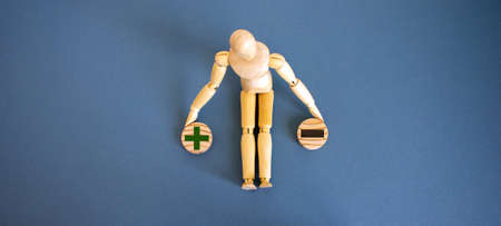 Wooden model of a man seats near 2 small wooden circles with signs plus and minus. Business concept.の写真素材