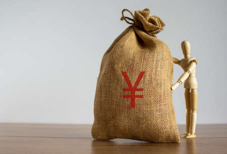 Wooden model of a man near large canvas bag with a Japanese yen sign.の写真素材