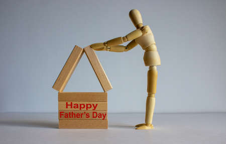 Wooden man builds a model of a wooden house. Lettering 'Happy Father's Day'. Concept image.の写真素材