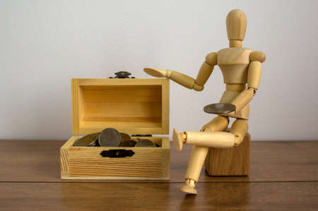 Wooden model of a man seats near small wooden coin chest.