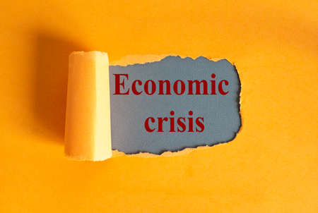 The text economic crisis appearing behind torn yellow paper.の写真素材