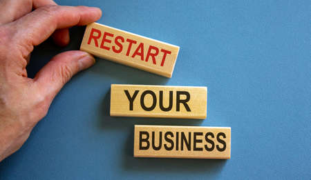 Wooden blocks form the words 'restart your business' on blue background. Male hand.の写真素材