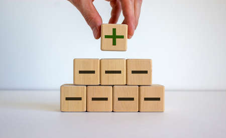 Male hand placing a cube with plus sign on top of a pyramid with minus signs.の写真素材