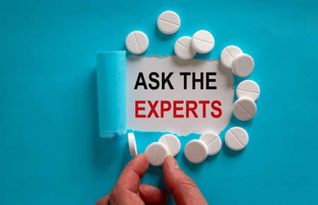 The text 'ask the experts' appearing behind torn blue paper. White pills and male hand. Beautiful blue and white background.の写真素材