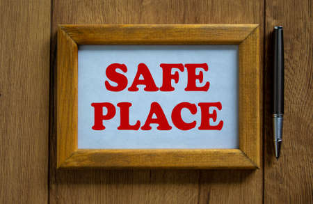Wooden picture frame with inscription 'safe place' on beautiful wooden background. Pen on the table. Concept.の写真素材