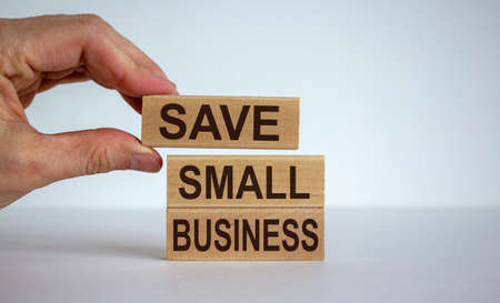 Male hand placing a blocks with word 'save' on top of a blocks tower with words 'small business'. Beautiful white background.の写真素材
