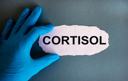 Hand in blue glove with white small paper. Concept word 'cortisol'. Blue background.の写真素材