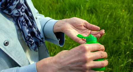 A woman treats her hands with a sanitizer. Green grass on the background. COVID-19 Pandemic Coronavirus concept.の写真素材