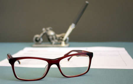 Glasses lying on the document. Pen in a stand in the shape of a motorcycle. Image of the objects typical for business environment.の写真素材