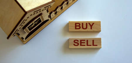 Wooden blocks form the words 'buy sell' near miniature house.の写真素材