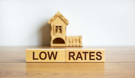 Wooden blocks form the words 'low rates' near miniature house. Wooden table. Beautiful white background, copy space.の写真素材