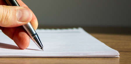 Notebook and fingers of a working man with a pen on wood table.の写真素材