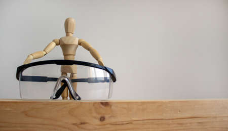 Safety glasses on a wooden bar. Wooden model of human. Beautiful white background. Copy space.の写真素材