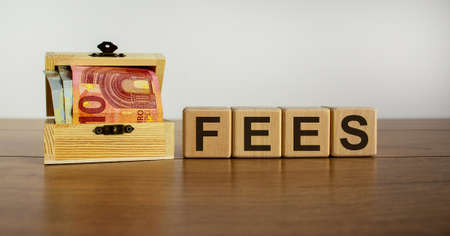 Concept word 'fees' on cubes on a beautiful wooden table, small chest with euro bills. Beautiful background. Copy space.の写真素材