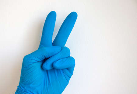 Doctor hand in sterile blue gloves. Sign victory from fingers. White background.の写真素材