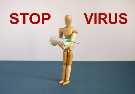COVID-19 Pandemic Coronavirus concept. Wooden model of a man holding a syringe. Text 'stop virus'. Beautiful white background.の写真素材