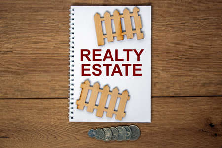 White note with inscription 'realty estate' on beautiful wooden table, metalic coins and miniature wooden fence. Business concept.の写真素材