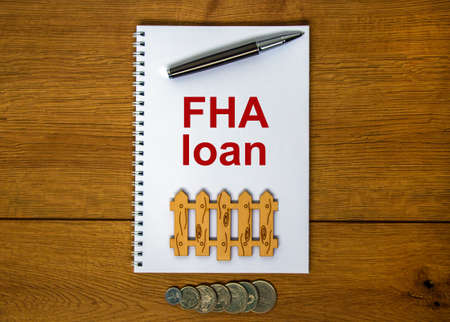 White note with inscription 'FHA loan' on beautiful wooden table, metalic pen, coins and miniature wooden fence. Business concept.の写真素材
