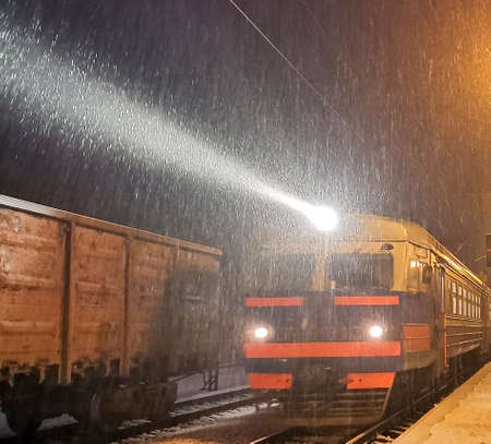 Evening train arrives at station. Snowfall complicates transportation of passengers, snow blockades. Blizzard and Snow driftsの写真素材