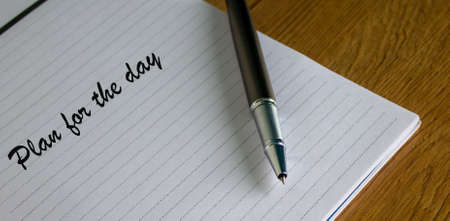 Notebook with the inscription plan for the day and pen on wood table.の写真素材